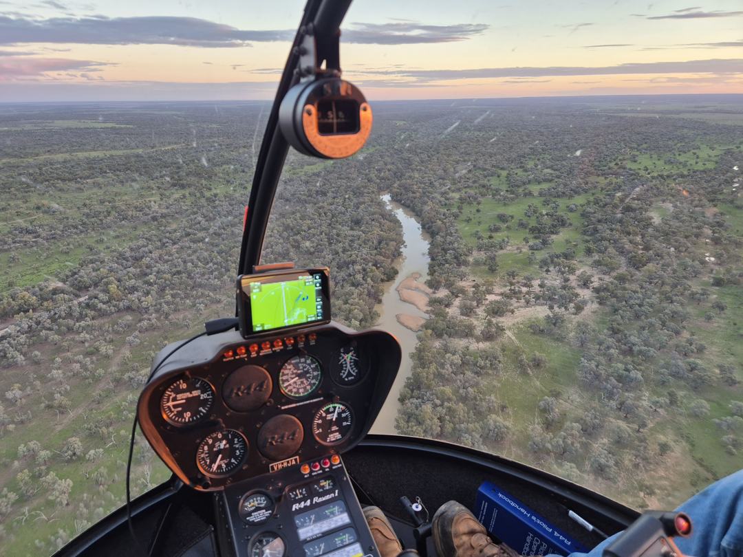 View from a helicopter cockpit over river country at dusk, with a GPS mapping tablet mounted on the instrument panel