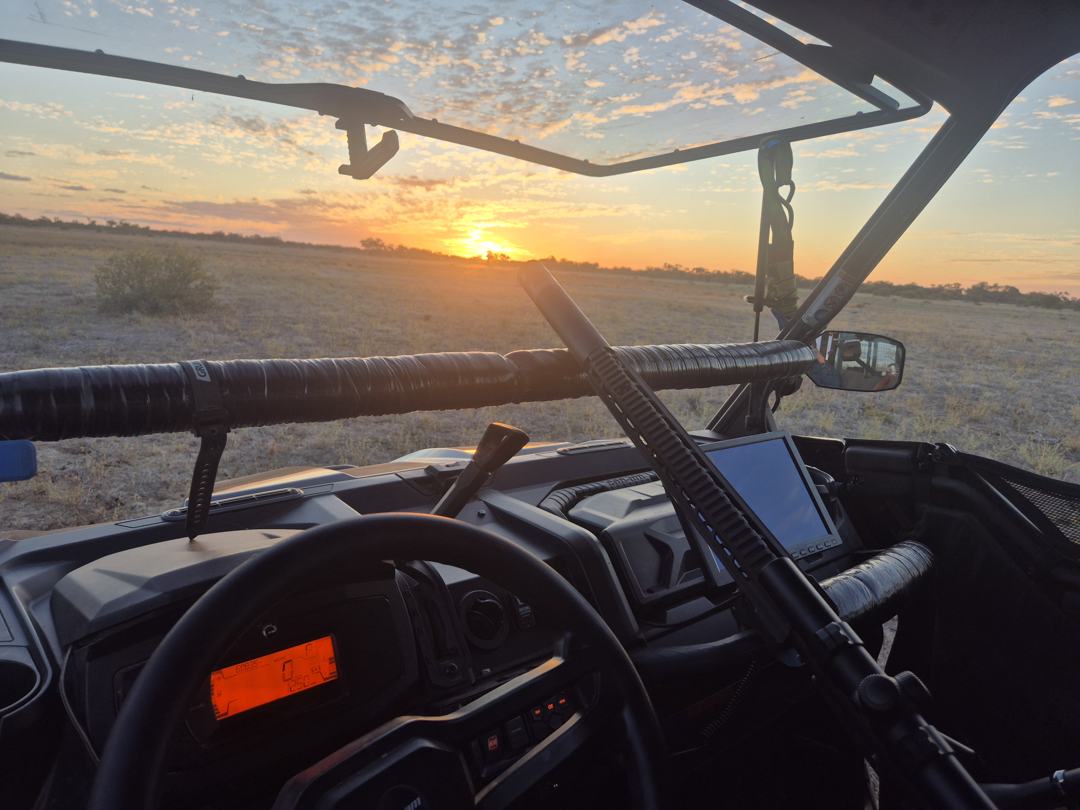 Inside a ground control vehicle at sunset, with a rifle stowed across the dash and a mounted screen